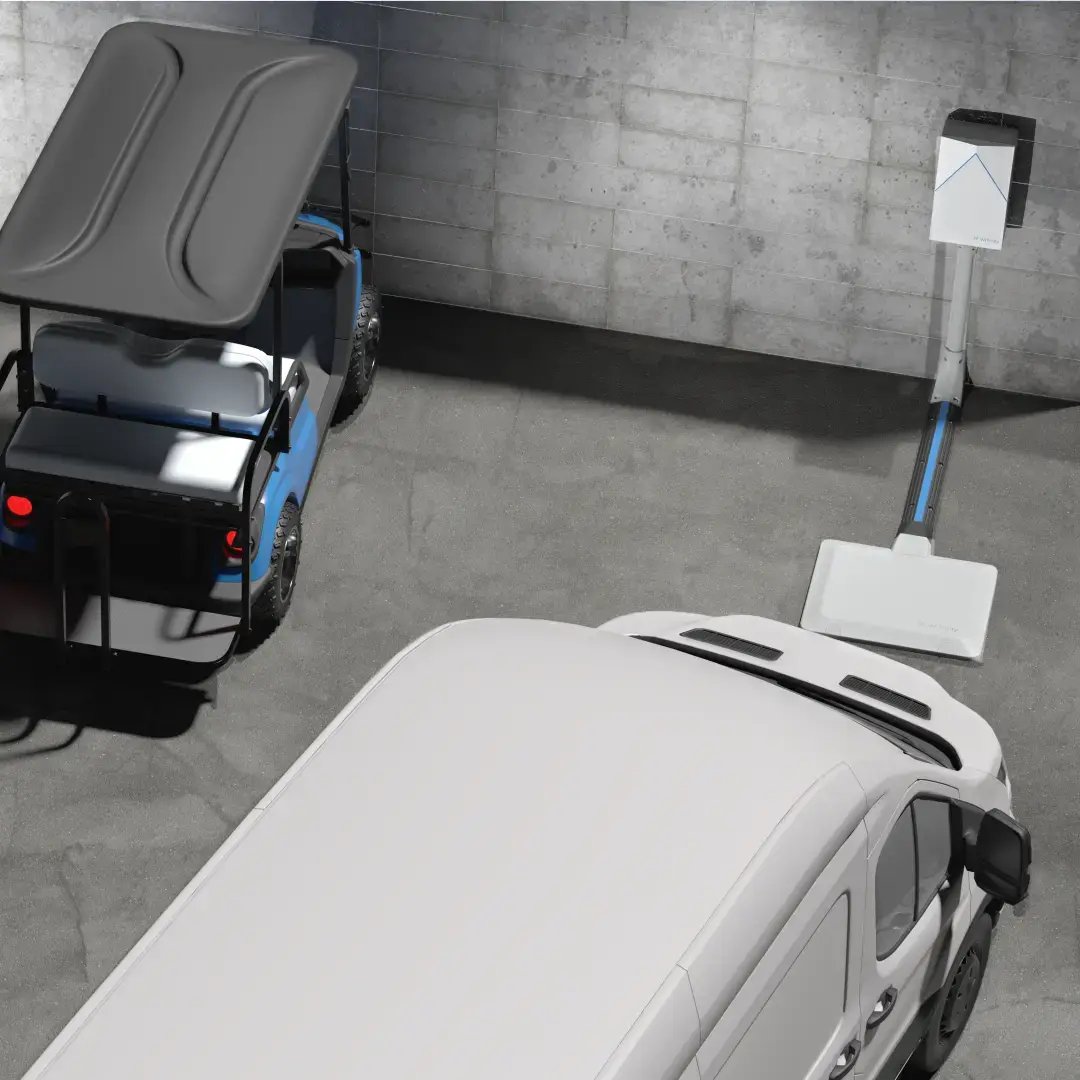 A white van approaches a wireless charging pad in an industrial parking lot while a utility cart is parked next to it charging.