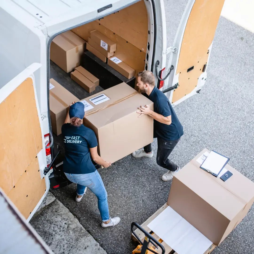 Two workers load a white delivery van with shipping boxes