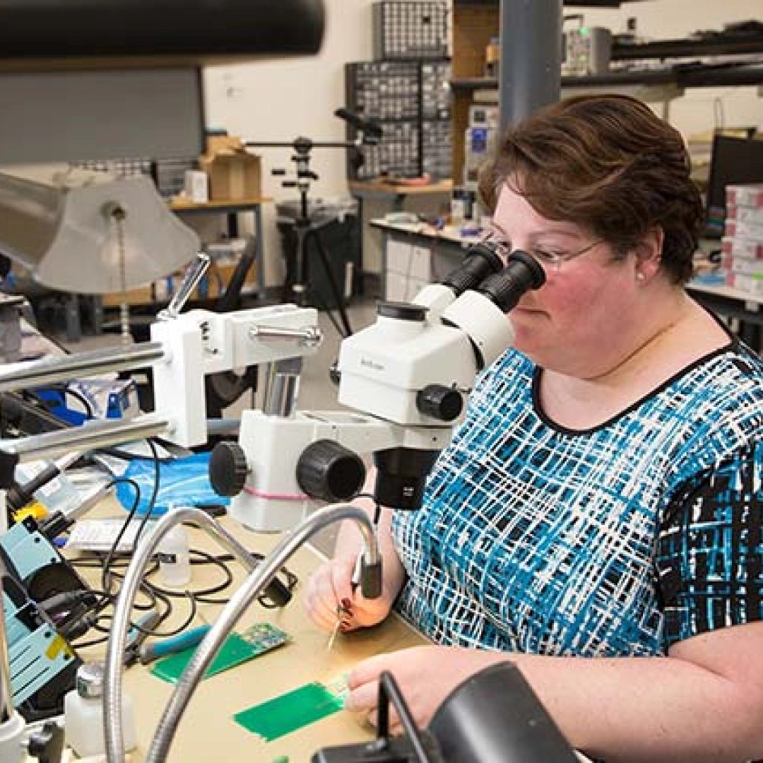 Lab technician inspects a PCB board using a microscope in a tech lab